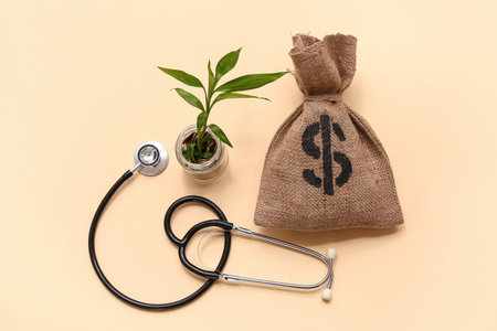 Jar with coins, plant, money bag and stethoscope on beige backgroundの写真素材
