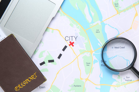 Laptop with passport and magnifier on city map. Itinerary concept