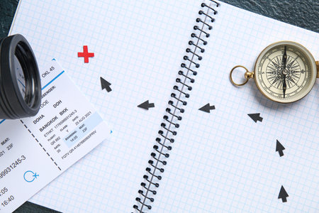 Notebook with compass and ticket on dark background, closeup. Itinerary concept