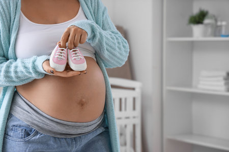 Young pregnant woman with baby booties in children's bedroom, closeup