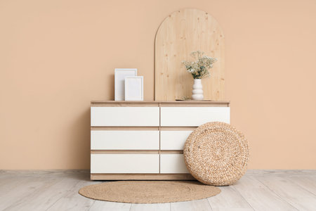 Chest of drawers with decor and gypsophila flowers in vase near beige wall in room