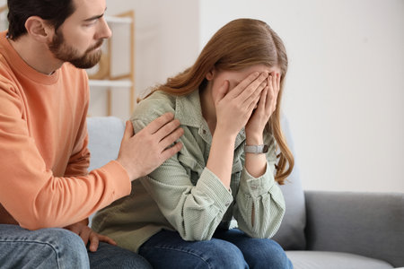 Young man apologizing to his crying wife on sofa at homeの写真素材