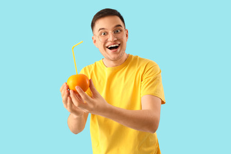 Young man holding orange with straw on blue backgroundの写真素材