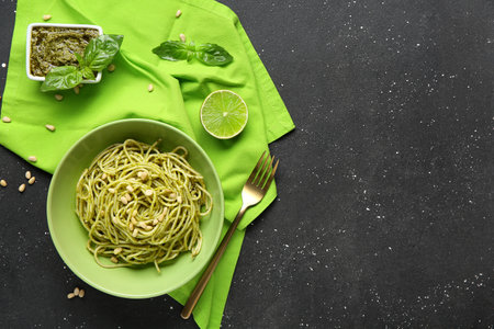 Plate with tasty pesto pasta, bowl of sauce and ingredients on black grunge backgroundの写真素材