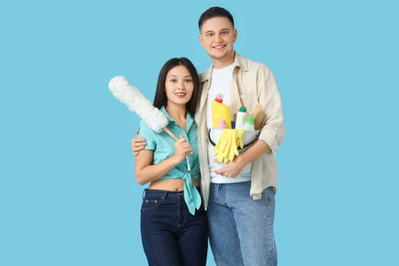 Cute young couple with cleaning supplies and pp-duster on blue backgroundの写真素材