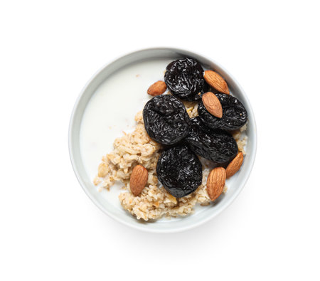 Bowl of tasty oatmeal with prunes, almonds and milk on white backgroundの写真素材