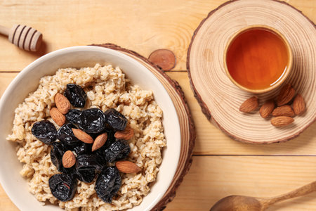 Bowl of tasty oatmeal with prunes, almonds and honey on light wooden backgroundの写真素材