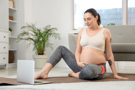 Young pregnant woman with laptop doing yoga at homeの写真素材