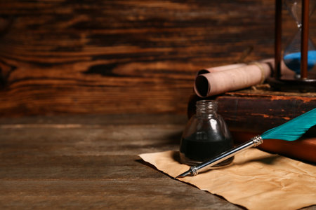 Old books with nib pen, inkwell, scrolls and hourglass on wooden background