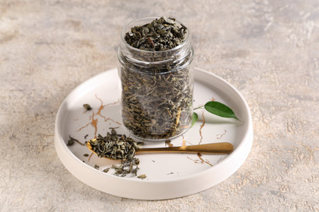 Jar and teaspoon with dried green tea leaves on white backgroundの写真素材