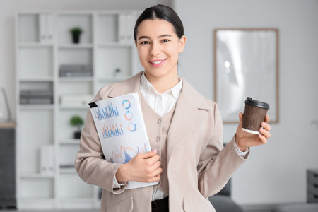Young businesswoman with coffee cup and report in officeの写真素材