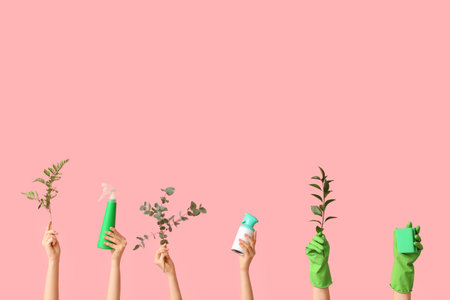 Female hands in rubber gloves with bottles of detergents, sponge and plant branches on pink backgroundの写真素材