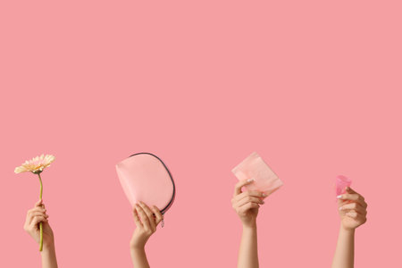Female hands with menstrual cup, pad and cosmetic bag on pink backgroundの写真素材
