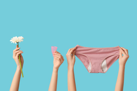 Female hands with period panties, menstrual cup and flower on blue backgroundの写真素材