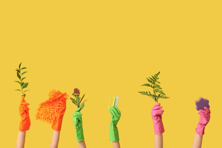 Female hands in rubber gloves with brushes and plant branches on yellow backgroundの写真素材