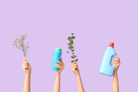 Female hands with bottles of detergents and plant branches on purple backgroundの写真素材