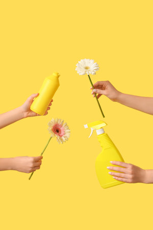 Female hands with bottles of detergents and flowers on yellow backgroundの写真素材
