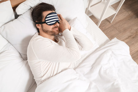 Handsome young man with sleep mask sleeping in bed at homeの写真素材