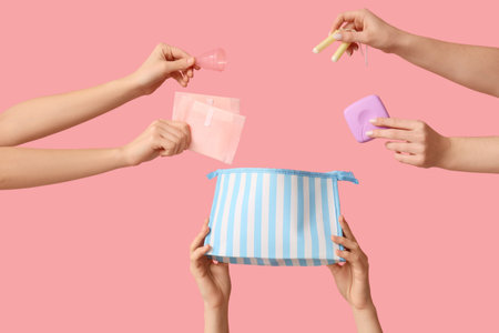 Female hands with cosmetic bag, menstrual cup, tampons storage box and pads on pink backgroundの写真素材