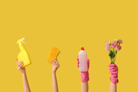 Female hands with bottles of detergents, sponges and flowers on yellow backgroundの写真素材