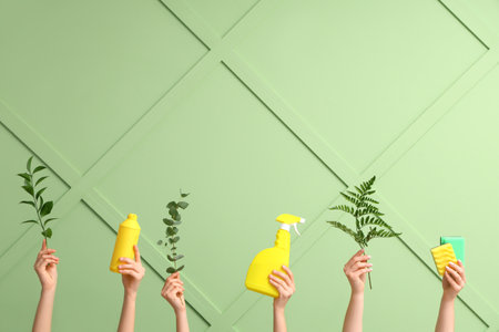 Many female hands with bottles of detergents, sponges and plant branches on green backgroundの写真素材