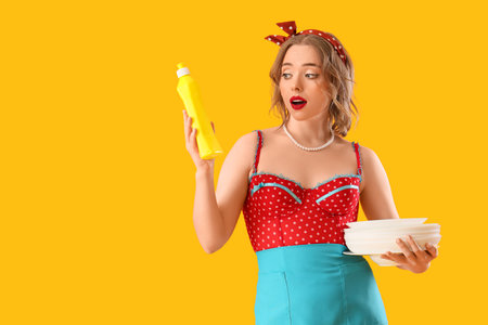 Shocked pin-up housewife with detergent and dishes on orange backgroundの写真素材