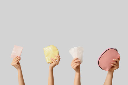 Female hands with cosmetic bags and menstrual pads on gray backgroundの写真素材