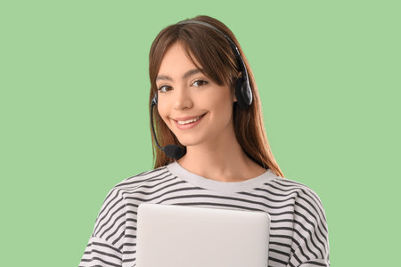Teenage girl in headset with laptop working online on green background, closeup