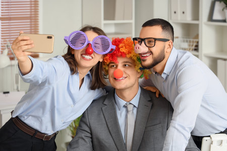 Young colleagues with funny disguise taking selfie in office. April Fools' Day celebrationの写真素材