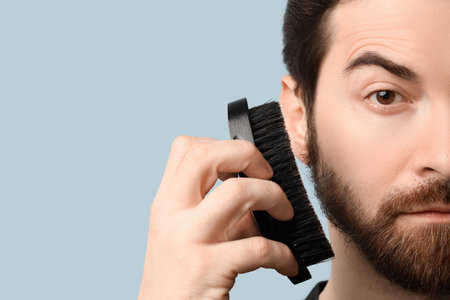 Handsome young man brushing his beard on blue background, closeupの写真素材