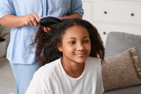 African-American mother brushing her happy daughter's curly hair at homeの写真素材