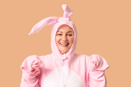 Funny senior woman in Easter bunny costume on beige backgroundの写真素材
