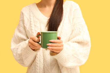 Young Asian woman with cup of hot tea on yellow background, closeupの写真素材