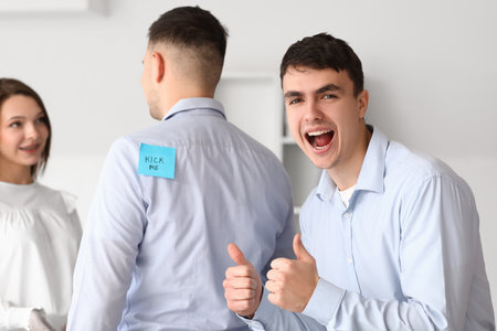 Young colleagues and man with sticky paper on his back in office. April Fools' Day celebrationの写真素材