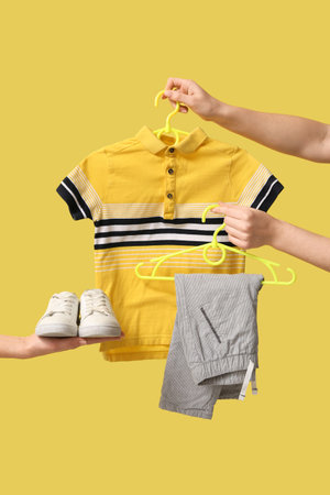Female hands with stylish children's clothes and shoes on yellow backgroundの写真素材