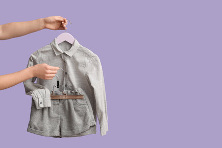 Female hands with stylish children's clothes on lilac backgroundの写真素材