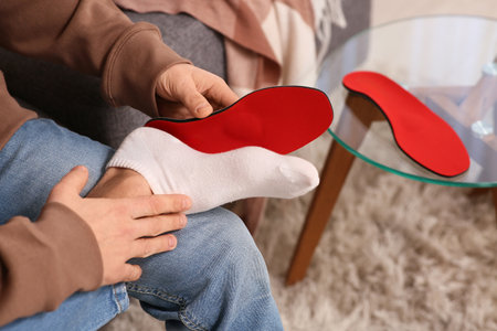 Young man applying orthopedic insole to his foot at home, closeupの写真素材