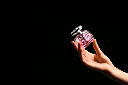 Female hand with pink bottle of perfume on black background