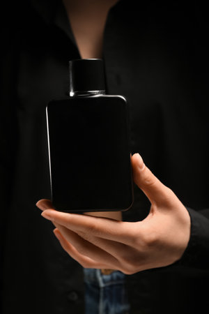 Young woman with black bottle of perfume as background, closeupの写真素材