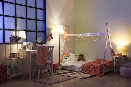 Interior of stylish children's bedroom with toys, cozy bed and glowing lamps at nightの写真素材
