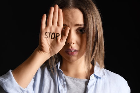 Young woman showing stop gesture on dark background, closeup. Domestic violence conceptの写真素材