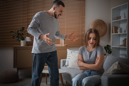 Bruised young woman with her angry husband at home. Domestic violence conceptの写真素材