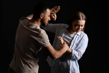 Man and woman in a physical altercation on dark background. Domestic violence concept