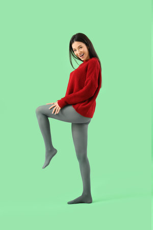 Young woman in sweater and tights on green backgroundの写真素材