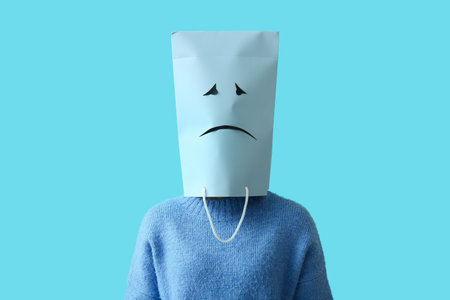 Woman and paper bag with drawn sad face on her head against blue backgroundの写真素材