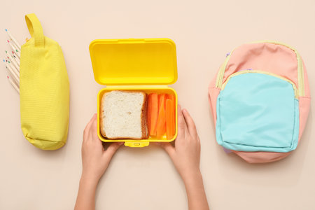 Child's hands with lunch box, backpack and pencil case on beige background. Top viewの写真素材