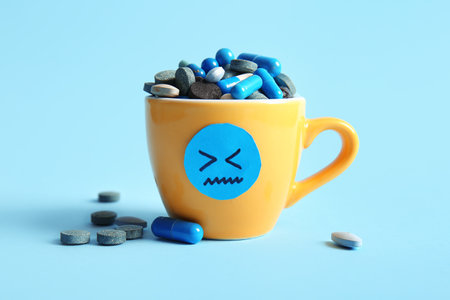 Cup with drawn sad face and pills on blue backgroundの写真素材