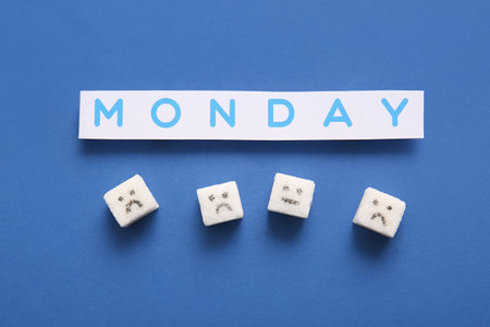 Word MONDAY and sugar cubes with drawn sad faces on blue backgroundの写真素材