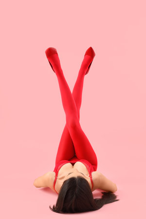 Young woman in red tights lying on pink backgroundの写真素材