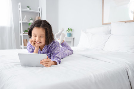Little Asian girl watching cartoons on tablet computer in bedroomの写真素材